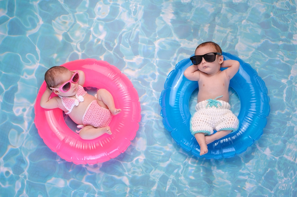 Zwei Kinder liegen auf jeweils einem Schwimmring in einem Pool. Der eine Ring ist rosa. Der andere babyblau. 